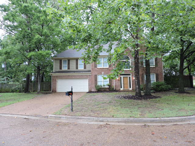 a brick house with a driveway and trees
