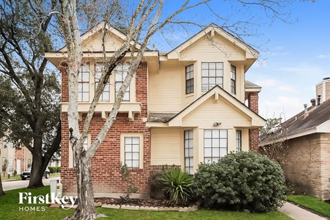 a brick and cream colored house with a tree in front of it
