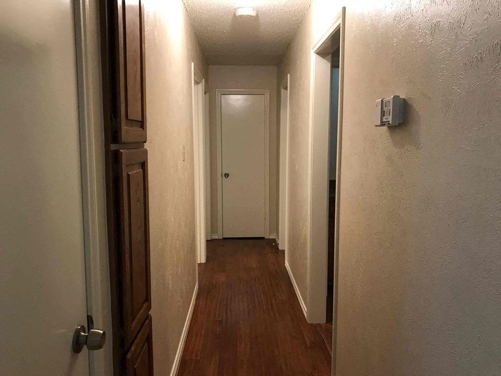 a hall way with a door to a room and a hallway with a wood floor