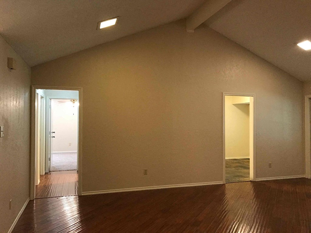 an empty living room with wooden floors and a door to a hallway