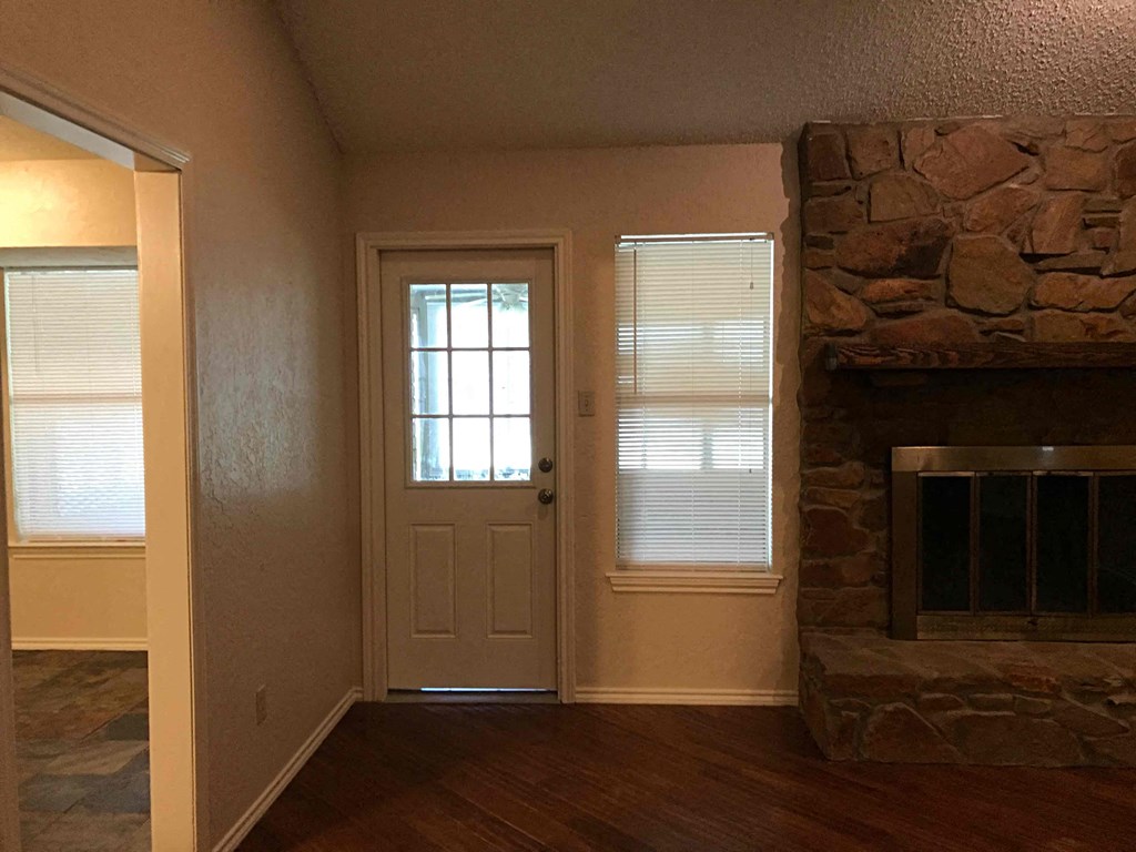 an empty living room with a stone fireplace and a door