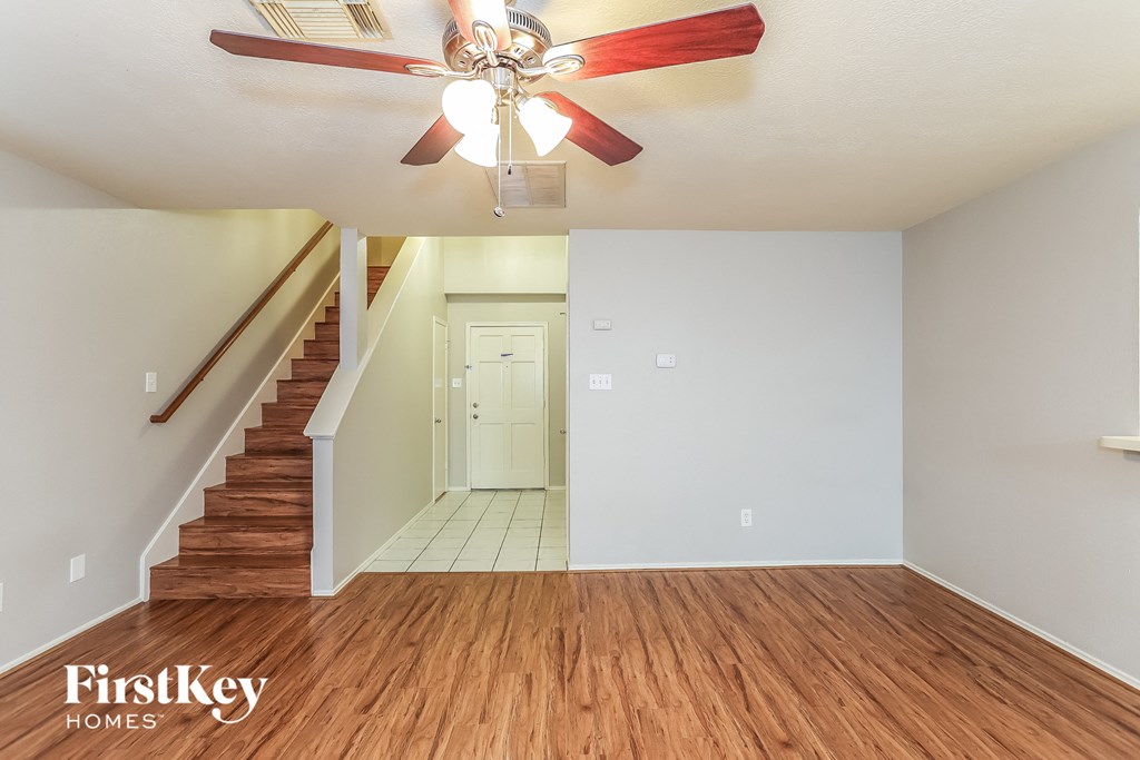 A wood floored room with a staircase and a ceiling fan.
