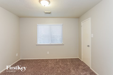 A room with a carpeted floor, a window with blinds, and a door.