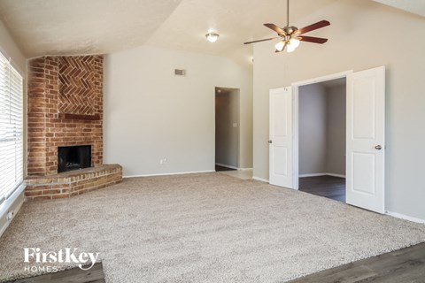 an empty living room with a brick fireplace and a ceiling fan