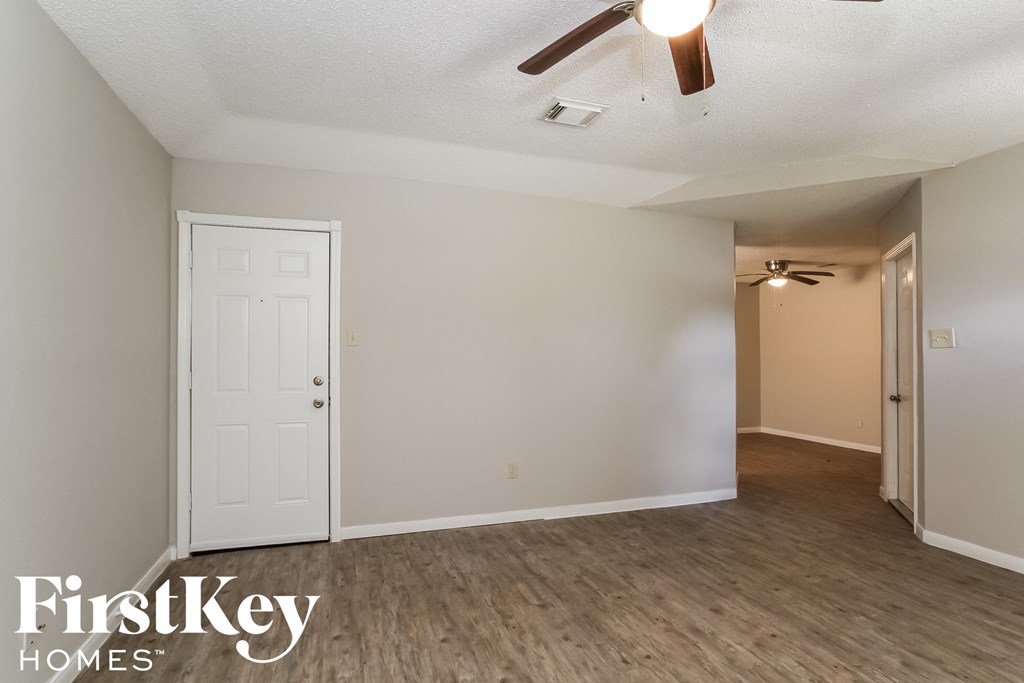an empty living room with a white door and a ceiling fan
