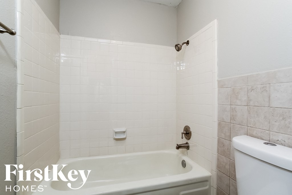 a white tiled bathroom with a tub and a toilet