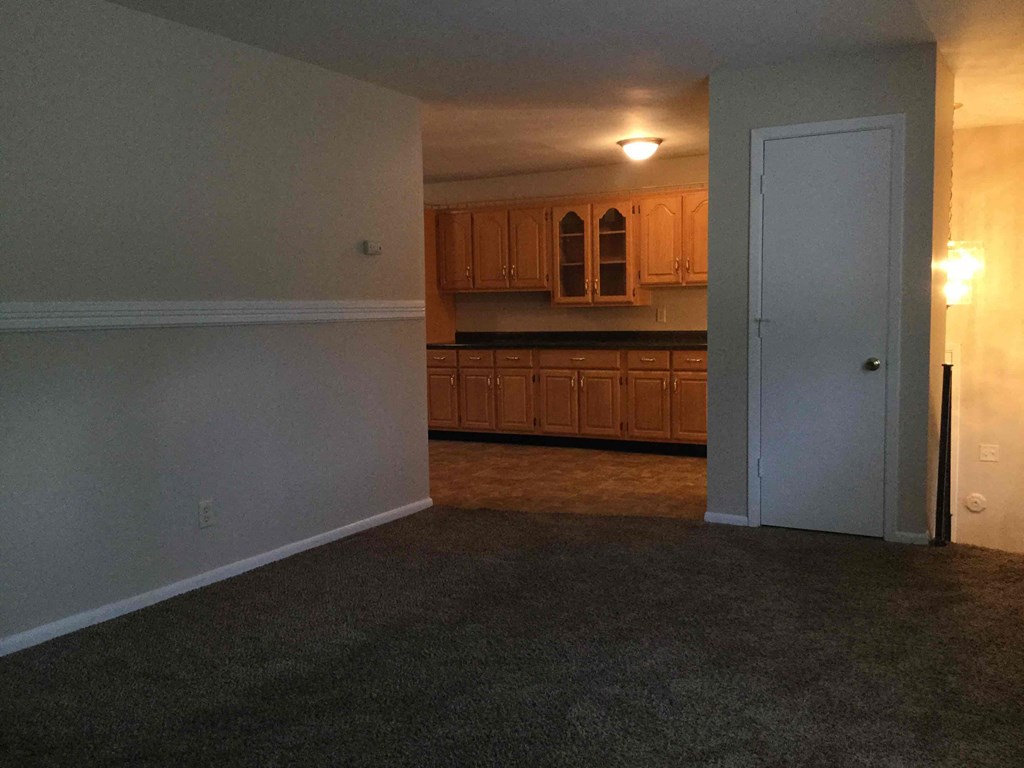 A room with a carpeted floor and a door leading to a kitchen.