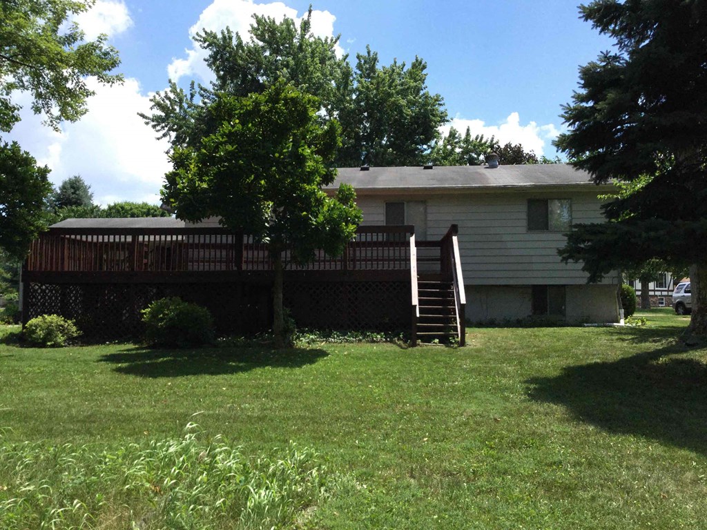 A house with a deck and a tree in front.