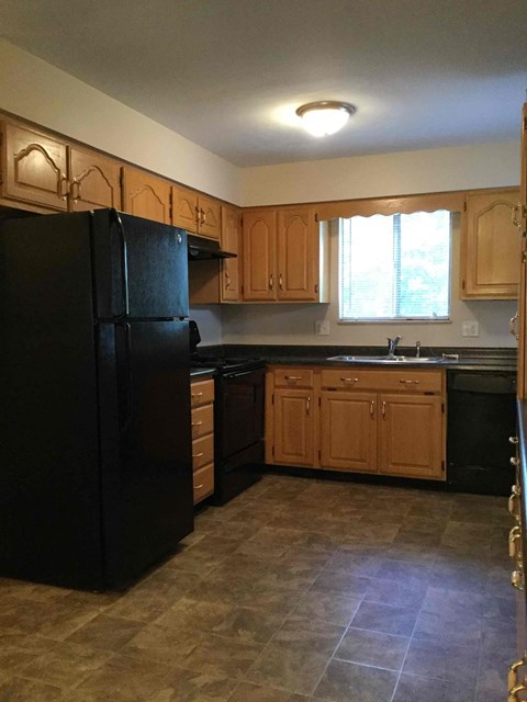 A black refrigerator in a kitchen with wooden cabinets.