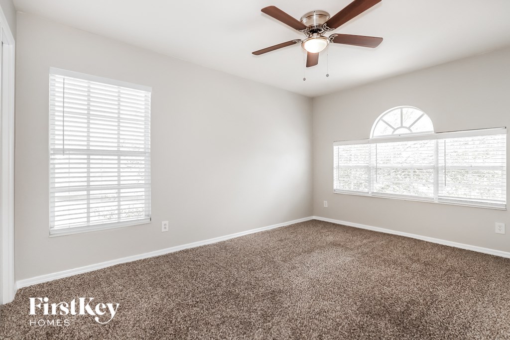 an empty room with a ceiling fan and two windows