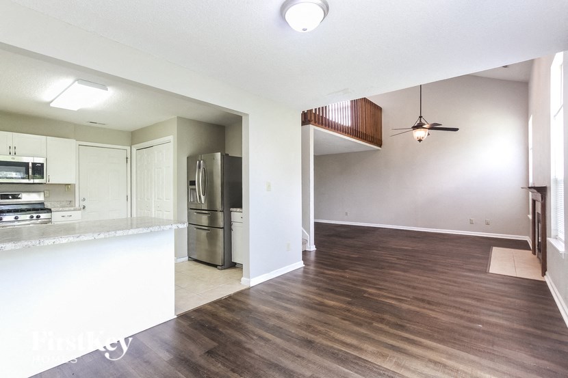 an empty living room with a kitchen and a stainless steel refrigerator