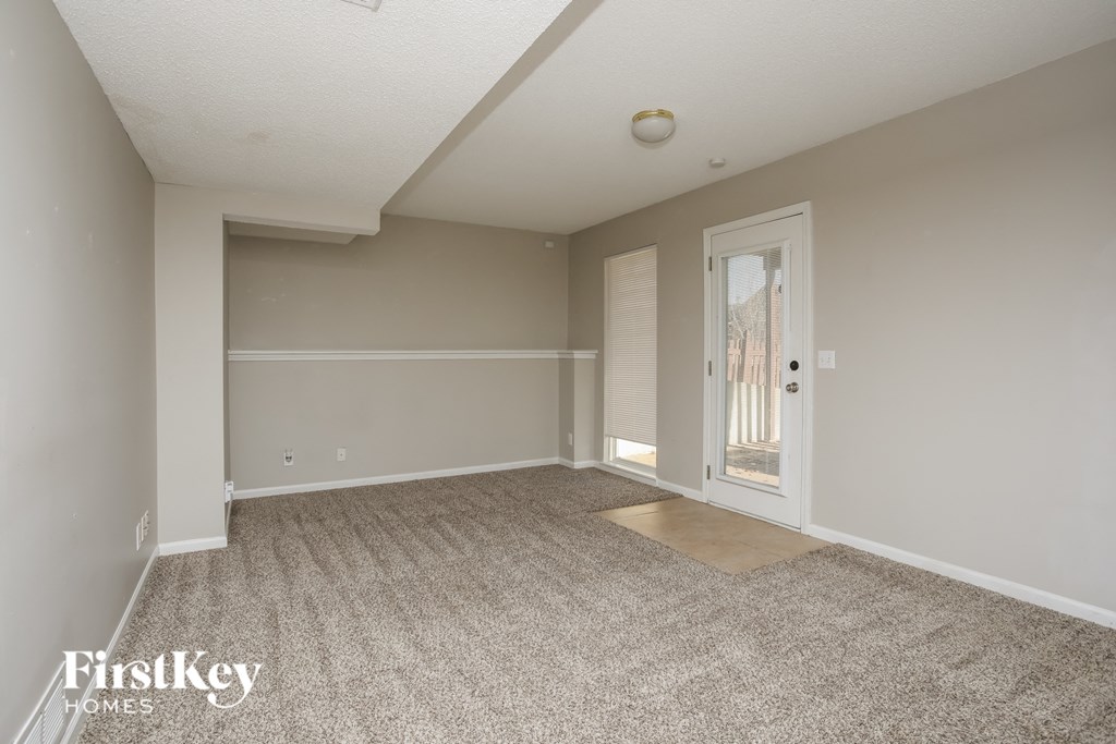 A spacious room with a carpeted floor and a door leading to another room.