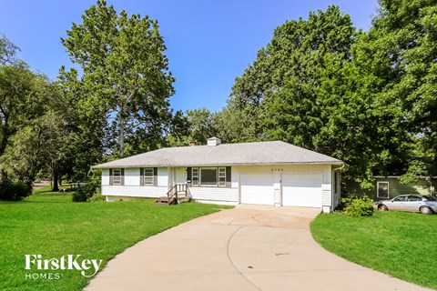 A house with a garage is surrounded by trees and has a clear blue sky above it.