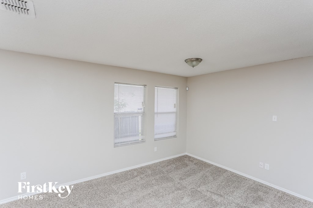 a spacious bedroom with carpet and two windows