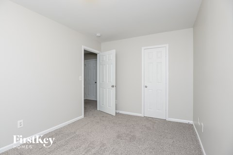 A white bedroom with two doors and a carpeted floor.