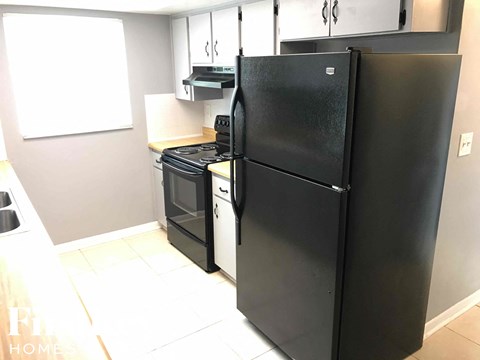 A black refrigerator stands in a kitchen with a white oven and stove.