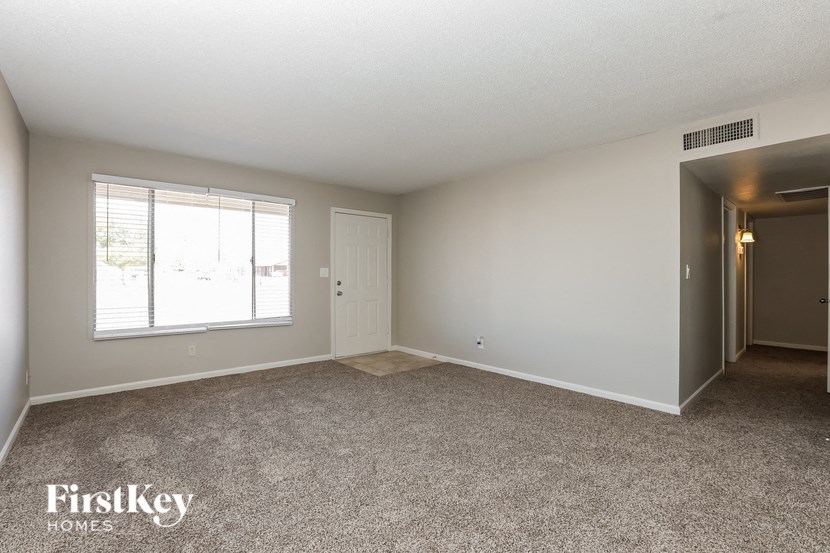the living room of an apartment with carpet and a window