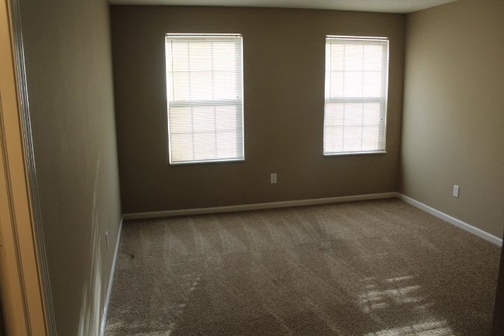 an empty room with two windows and a carpet