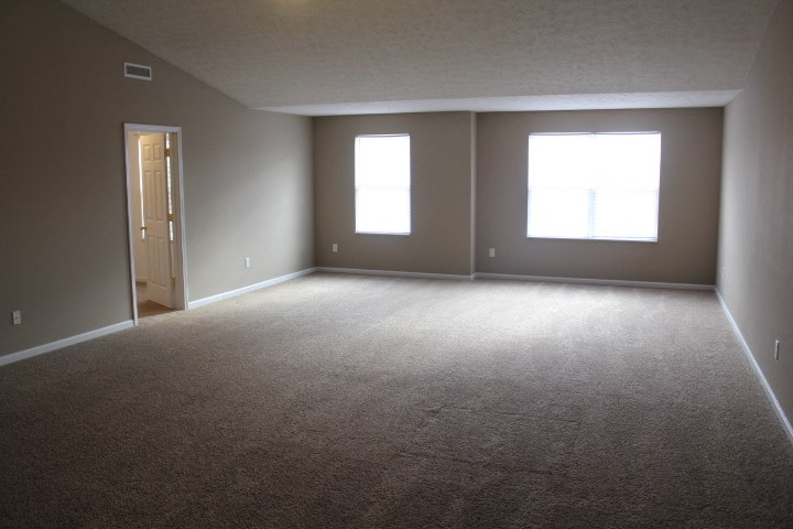 an empty living room with a door and two windows