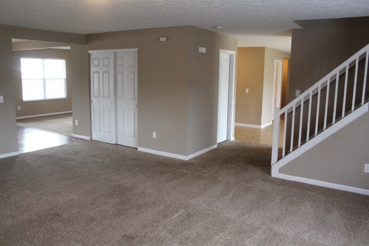an empty house with a carpeted living room and a staircase