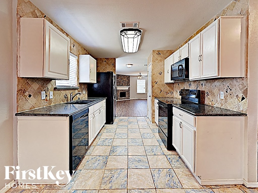 A kitchen with a black refrigerator and black countertops.