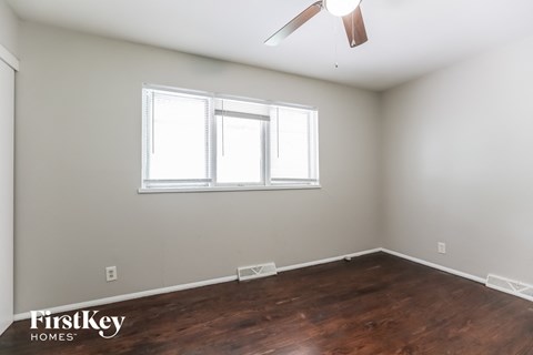 a bedroom with wood flooring and a window and a ceiling fan