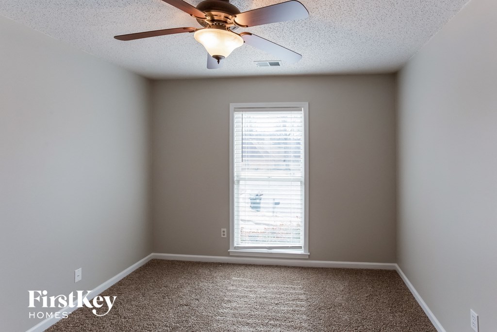A room with a carpet floor, a ceiling fan, and a window with blinds.