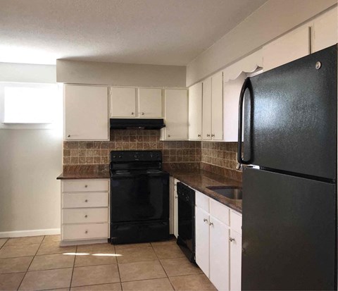 A black refrigerator is in a kitchen with white cabinets.