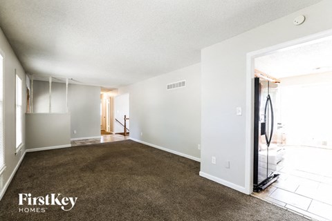 A spacious empty room with a carpet floor and a doorway leading to another room.