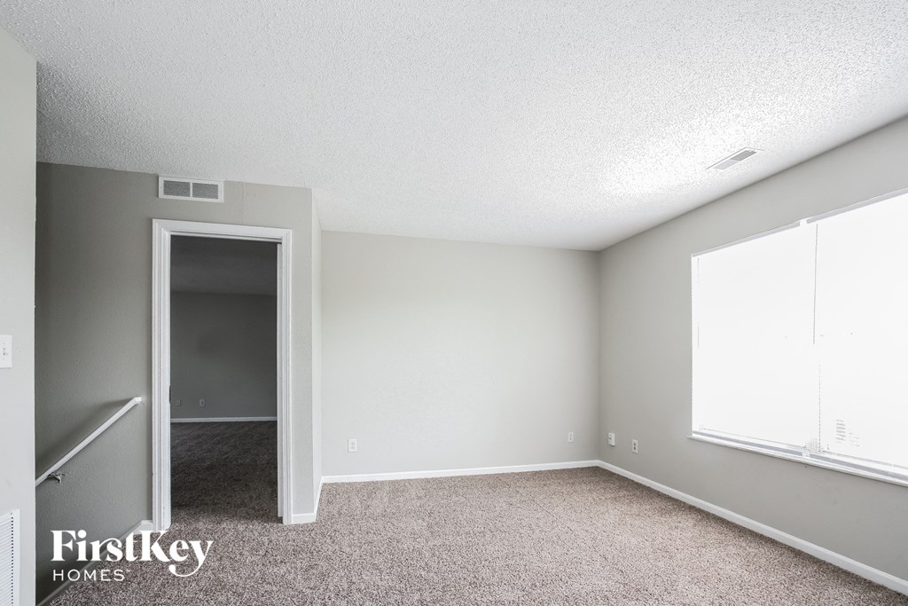 the living room of an apartment with carpet and a door to the hallway