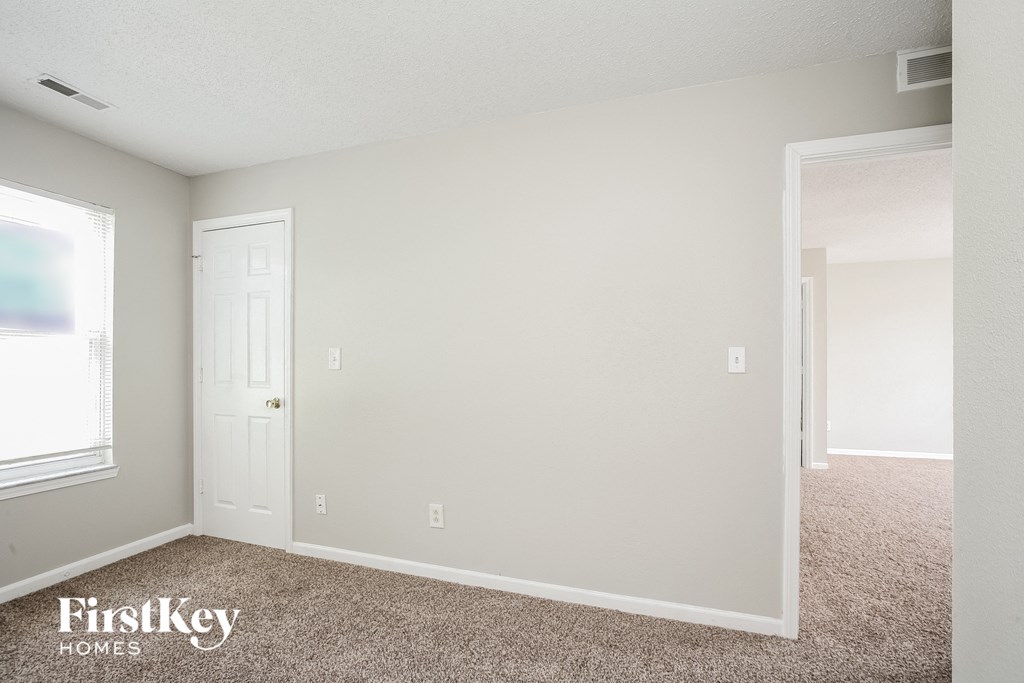a bedroom with white walls and carpet and a door to a closet