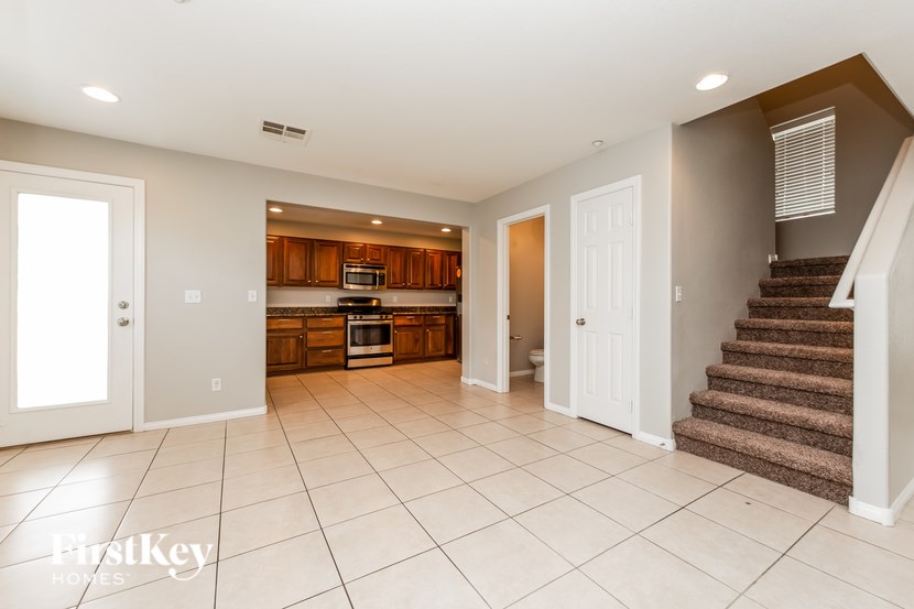 A spacious kitchen and living room with white tile flooring and wooden cabinets.