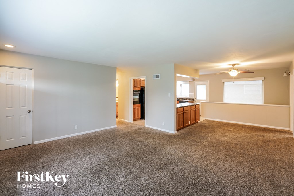 A spacious living room with a carpeted floor and a ceiling fan.