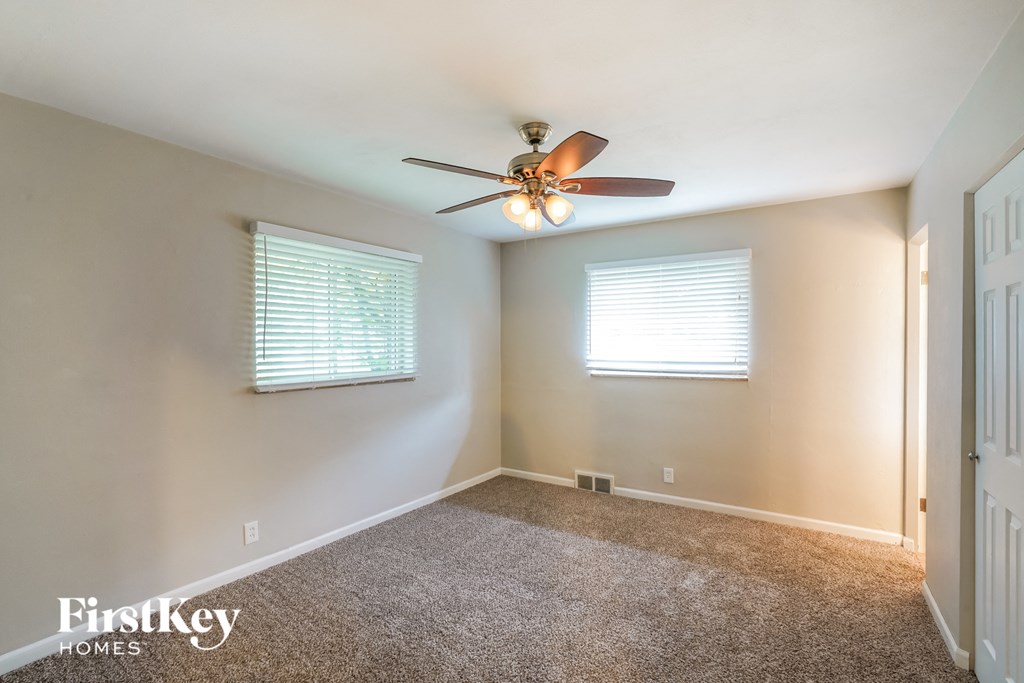 A room with a carpet floor, a ceiling fan, and two windows with blinds.