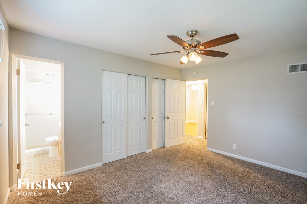 A carpeted room with a ceiling fan and three doors.