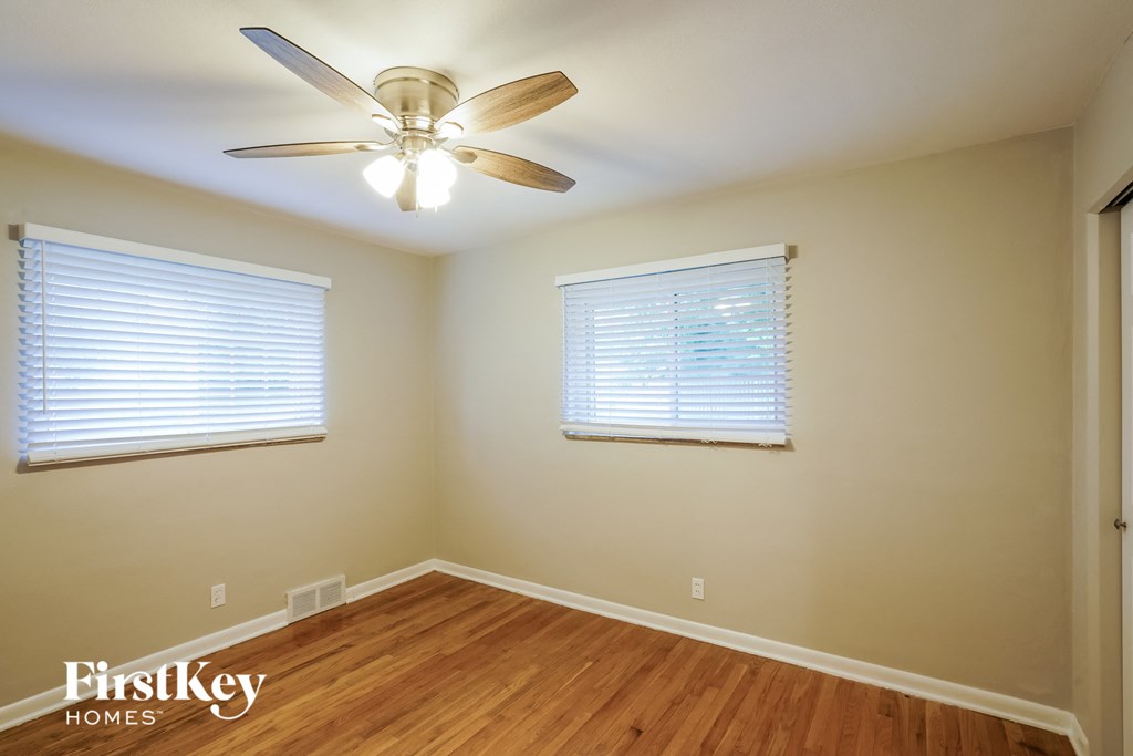 A room with a ceiling fan and two windows.