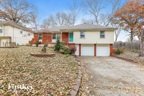 a white house with a driveway and a yard with fallen leaves