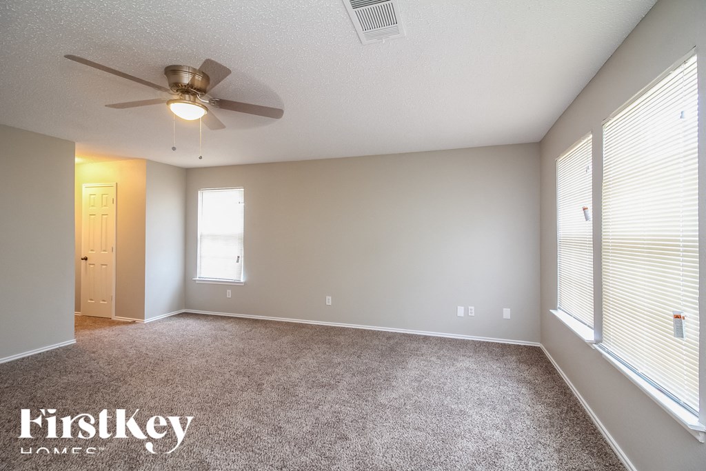 the spacious living room with large windows and a ceiling fan