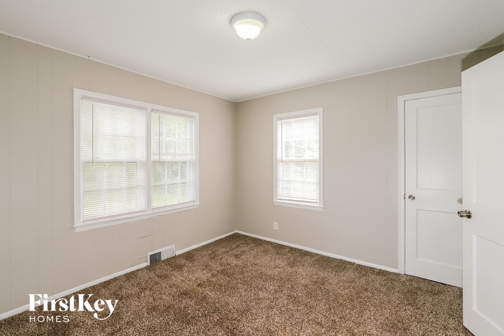 a bedroom with carpet and two windows and a door