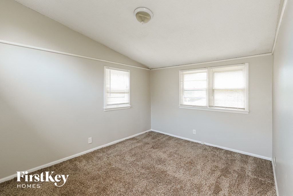 an empty room with carpet and two windows