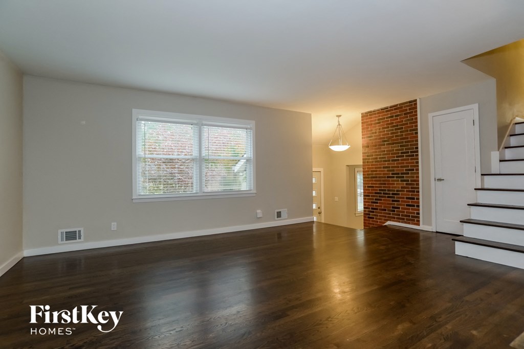 the living room and entryway of an empty house with wood floors and a staircase