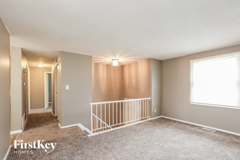 A spacious room with a carpeted floor and a window with white blinds.