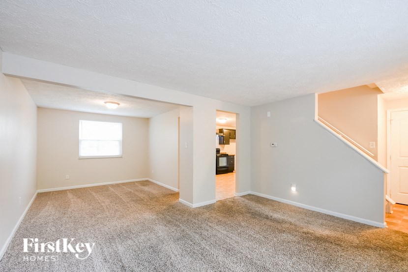 A spacious empty room with a carpeted floor and a staircase leading to another room.