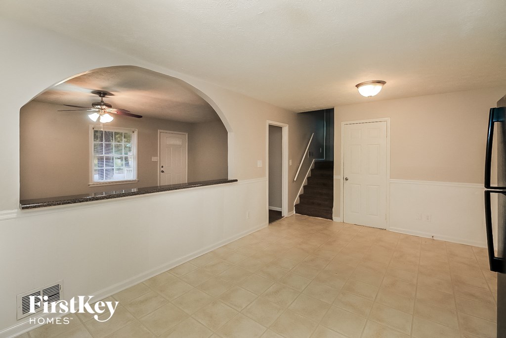 an empty living room with a kitchen and a hallway with a staircase
