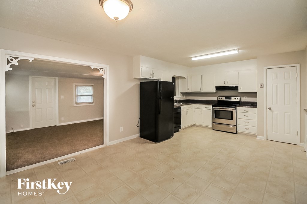 an empty kitchen with white cabinets and a black refrigerator