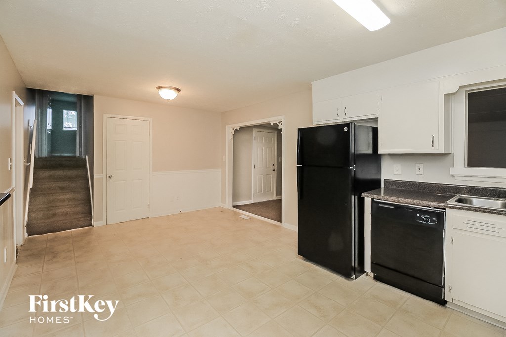 an empty kitchen and living room with a black refrigerator and dishwasher