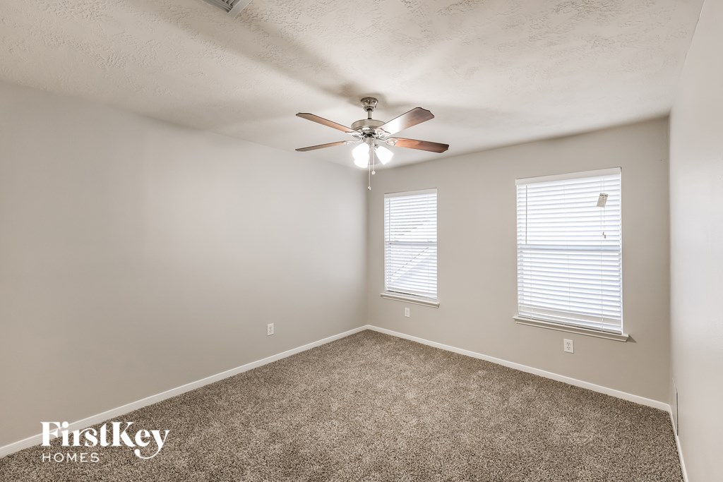 A room with a carpet floor, a ceiling fan, and two windows with blinds.