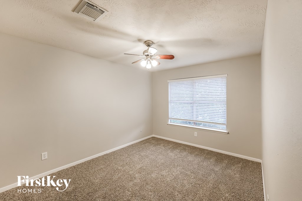 A room with a carpet floor, a ceiling fan, and a window with blinds.