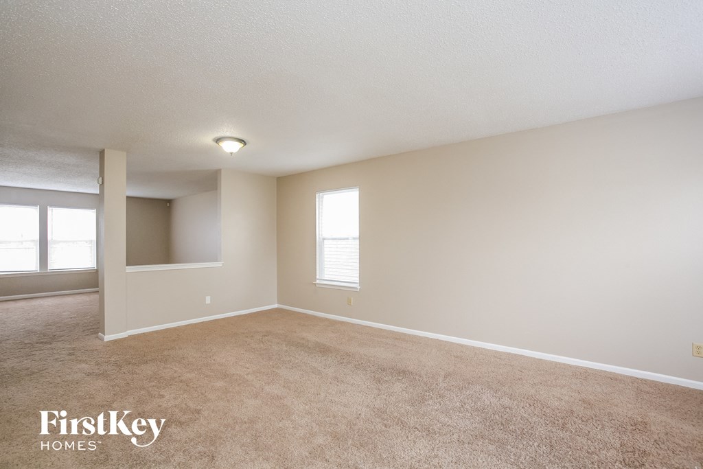 A spacious room with a carpeted floor and two windows.