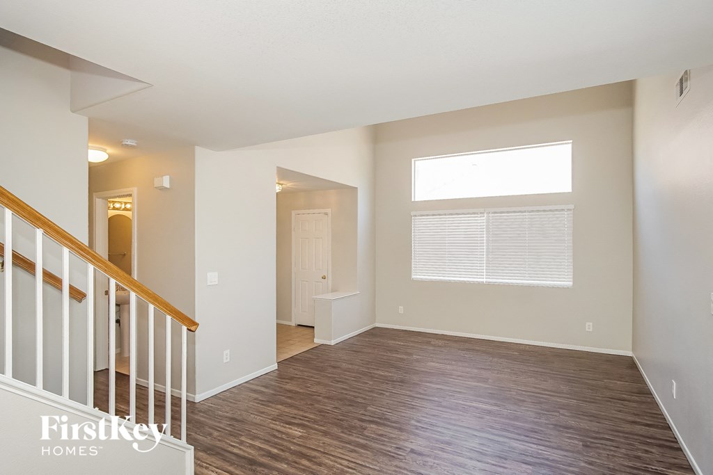 A spacious room with wooden flooring and a staircase with white railings.